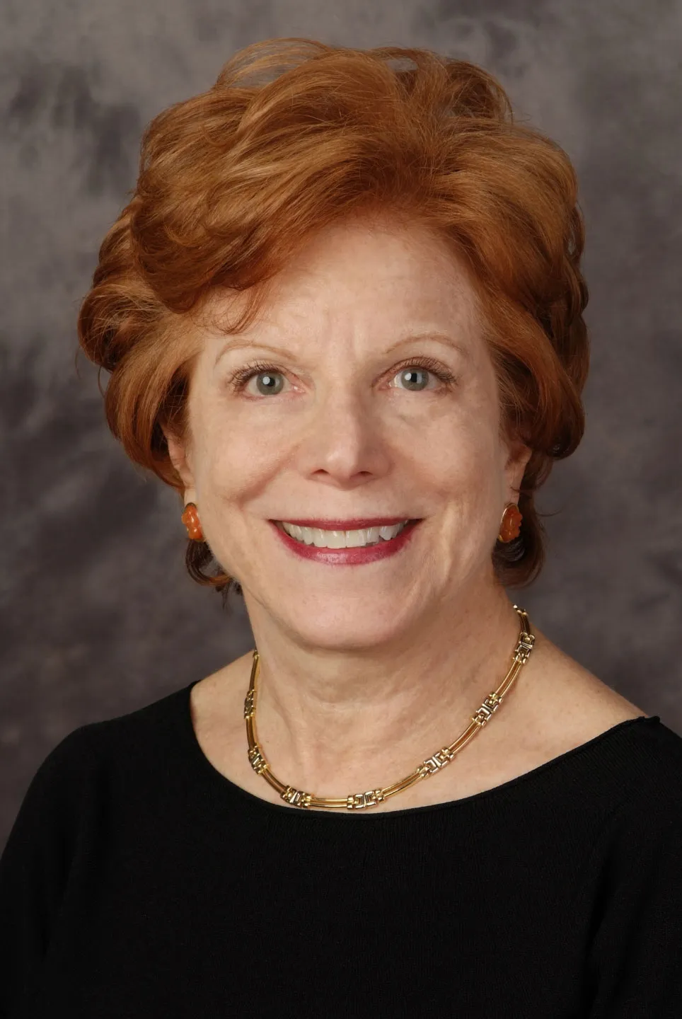Portrait of Mary Falvey, smiling, with auburn hair and a gold necklace