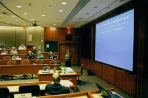 Mary Falvey presenting to a seated audience in a tiered business school lecture theatre