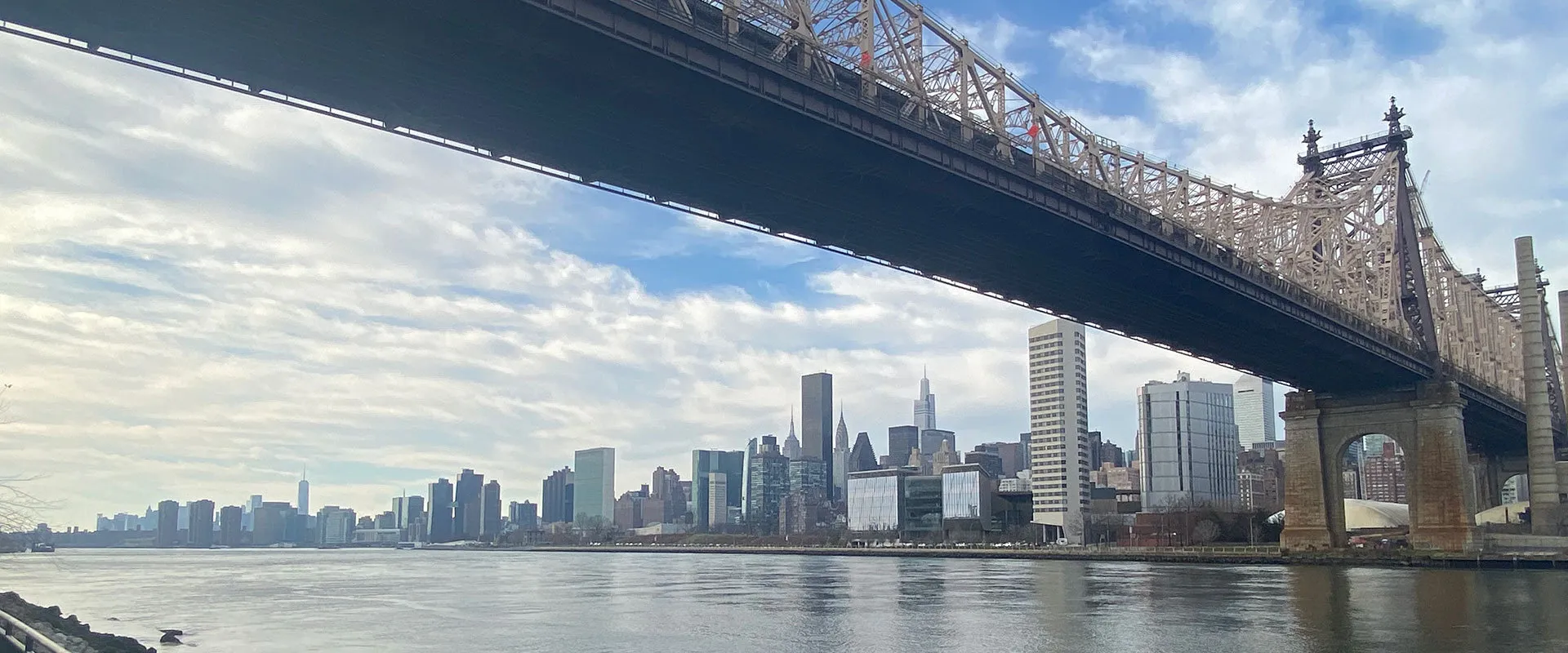 Manhattan skyline across the East River, seen from beneath the steel girders of the Queensboro Bridge